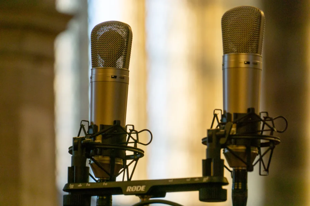 Close up image of a pair of large diaphragm condenser microphones on a stereo pair stand for recording a choir in a church hall.