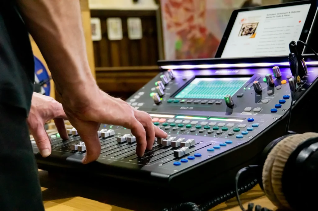 Photo showing a close up of our Allen & Heath SQ-5 mixing console and the hands of sound engineer Jamie Rhodes-Simpson, fingers on faders, mixing the Sanctuary Seekers Choir, Stories of Sanctuary concert at Leicester Cathedral.