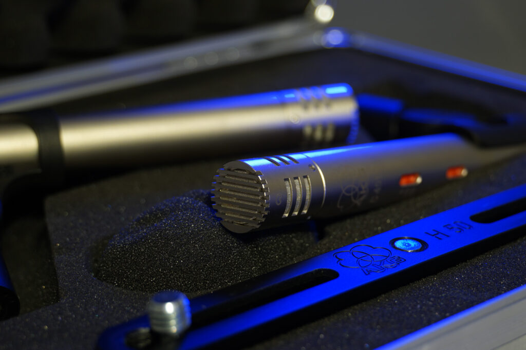 Shallow depth of field photograph of a matched stereo pair of AKG C451B small diaphragm condenser studio microphones positioned in their box with an AKG stereo bar also present.