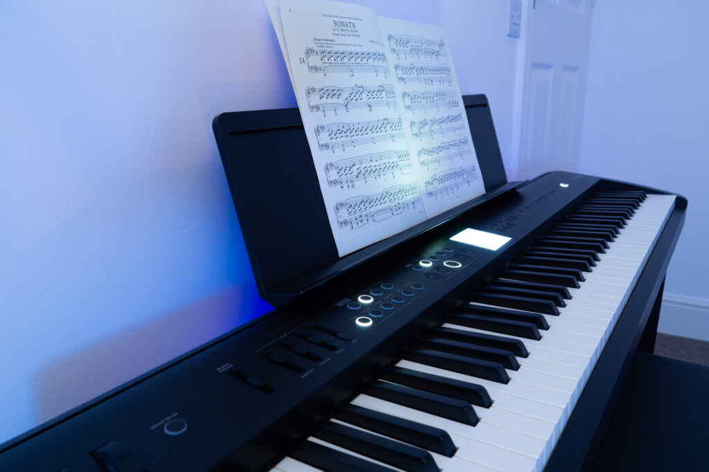 Close up shot of Roland FP-E50 digital piana taken looking up the keyboard from the low register end. Moonlight Sonata classical sheet music can be seen on the music stand.