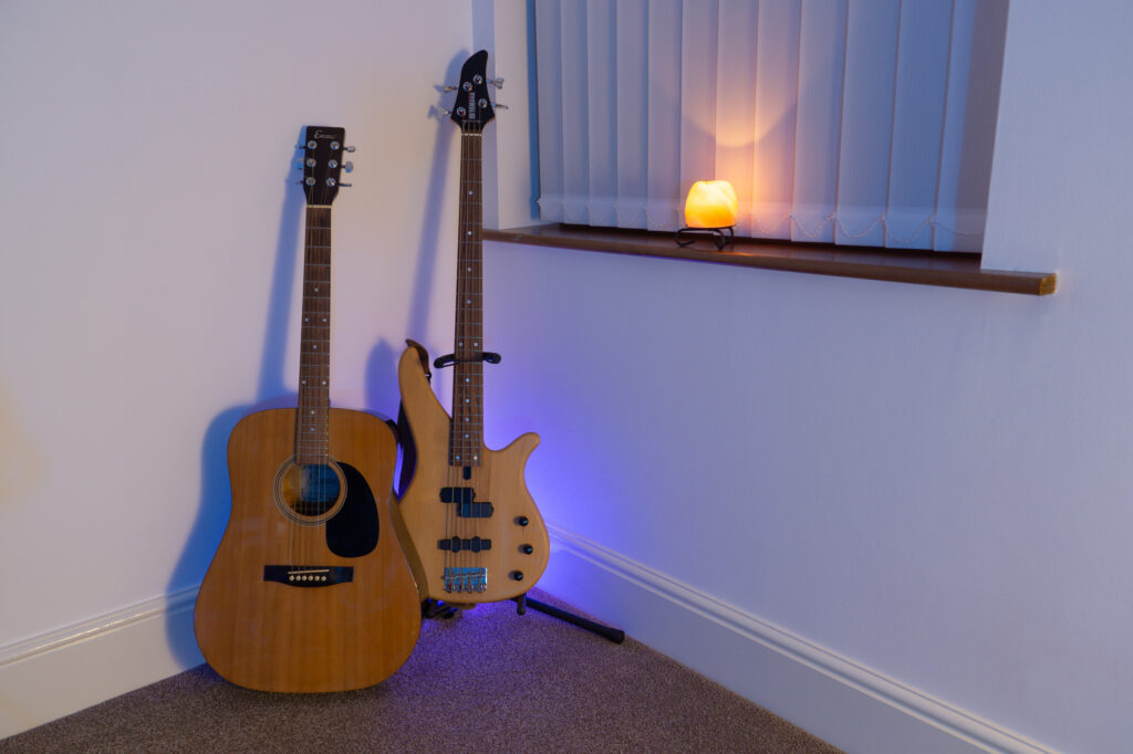 Photograph of a Yamaha electric bass guitar and an acoustic guitar in the Capybara Sound studio live room with a salt lamp emitting a nice glow on the nearby windowsill.