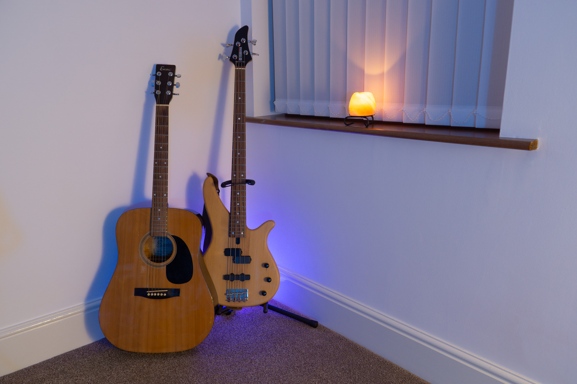 Photograph of a Yamaha electric bass guitar and an acoustic guitar in the Capybara Sound studio live room with a salt lamp emitting a nice glow on the nearby windowsill.