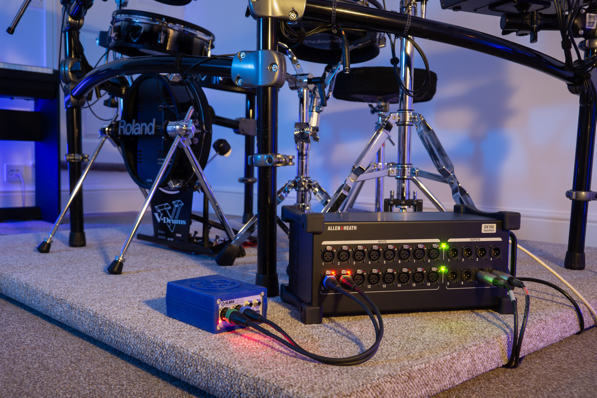 Close up photo of our Allen & Heath DX168 extender / stage box and a Klark Teknik DN200 DI box with Roland TD-20 drum kit in the background, all on a custom built drum riser in the Capybara Sound studio live room.