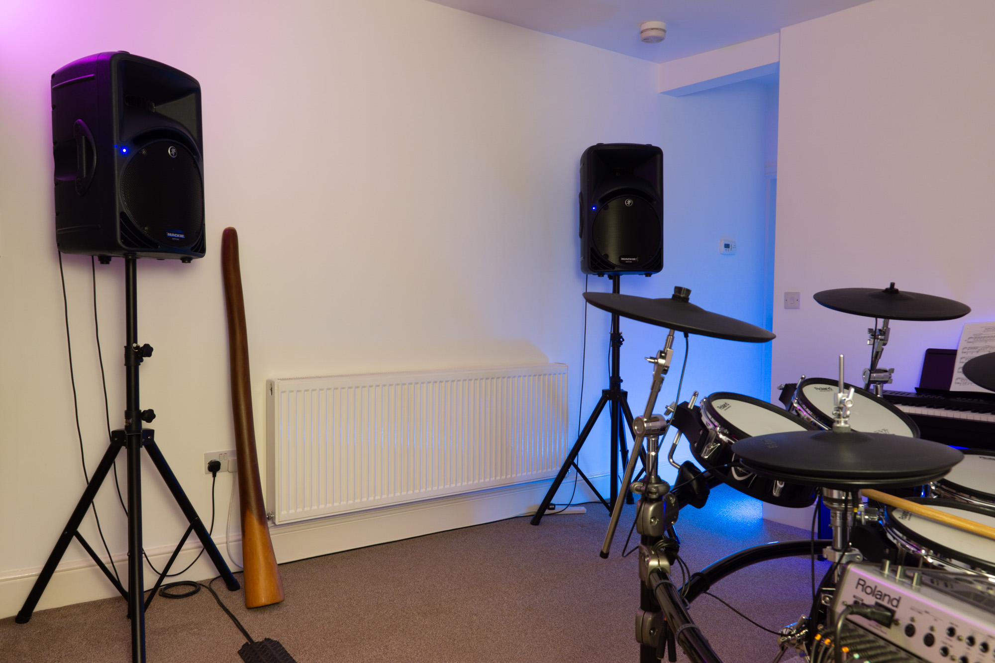 Photo of the Capybara Studio live room. A pair of Mackie SRM-450 speakers on stands can be seen against the wall with a didgeridoo and a the corner of a Roland TD-20 drum kit in the bottom left of the image capturing a few toms and cymbal trigger pads.