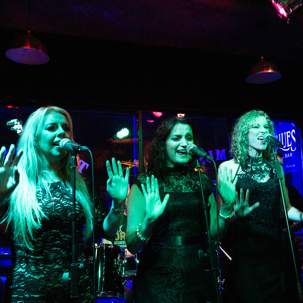 Photo of three female singers from Motown tribute act Detroit live, seen under green stage lights at Harrogate Blue Bar.