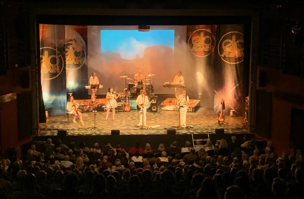 ELO Again performing on stage at The Lighthouse Theatre in Poole. ELO Again branded draps hang stage left and right. Electric violinist and cellist