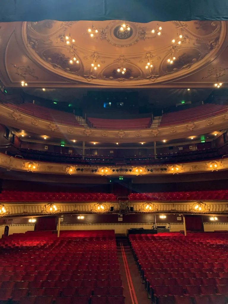 Photograph taken from the stage at Kings Theatre in Portsmouth by sound engineer Jamie Rhodes-Simpson showing the empty theatre with row after row of red velvet seats in the stalls plus three balcony levels. The roof is domed and painted gold.