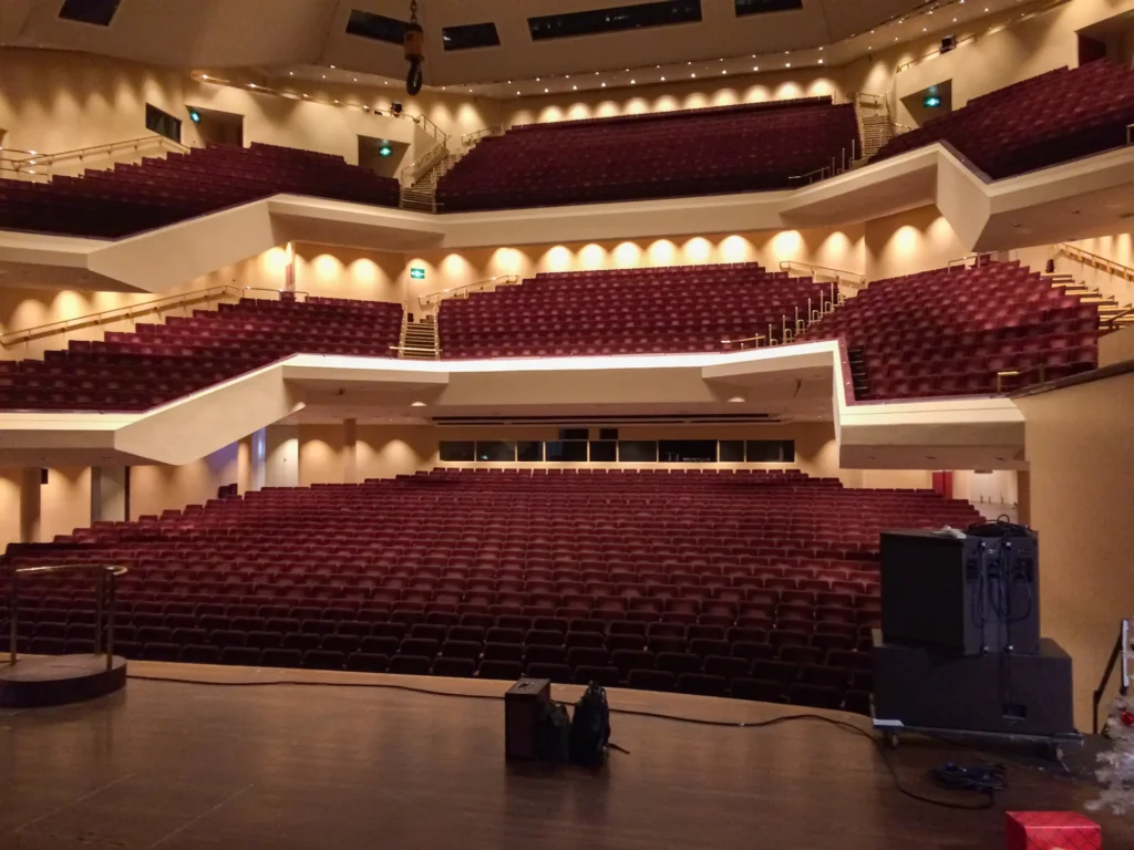 Photo taken from the stage when I (Jamie Rhodes-Simpson, sound engineer) arrived for the New Year’s Eve Sinfonia Viva concert at the Royal Concert Hall in Nottingham. The auditorium empty, house lights are on and over 2000 red velvet seats are in view. On the stage an L-Acoustics arc sound system can be seen. The concert later that evening is the full Sinfonia Viva orchestra led by conductor Nicholas Kok. Joining the orchestra were RPS Awards 2018 winning guitarist Sean Shibe, BBC Young Musician of the Year Keyboard finalist Jeneba Kanneh-Mason, Michael McIntyre’s Big Show star Andy Quinn, soprano Gabriella Cassidy and the Kristian Thomas Company performing choir duties in Freddie Mercury’s Barcelona and the finale, Auld Lang Syne.