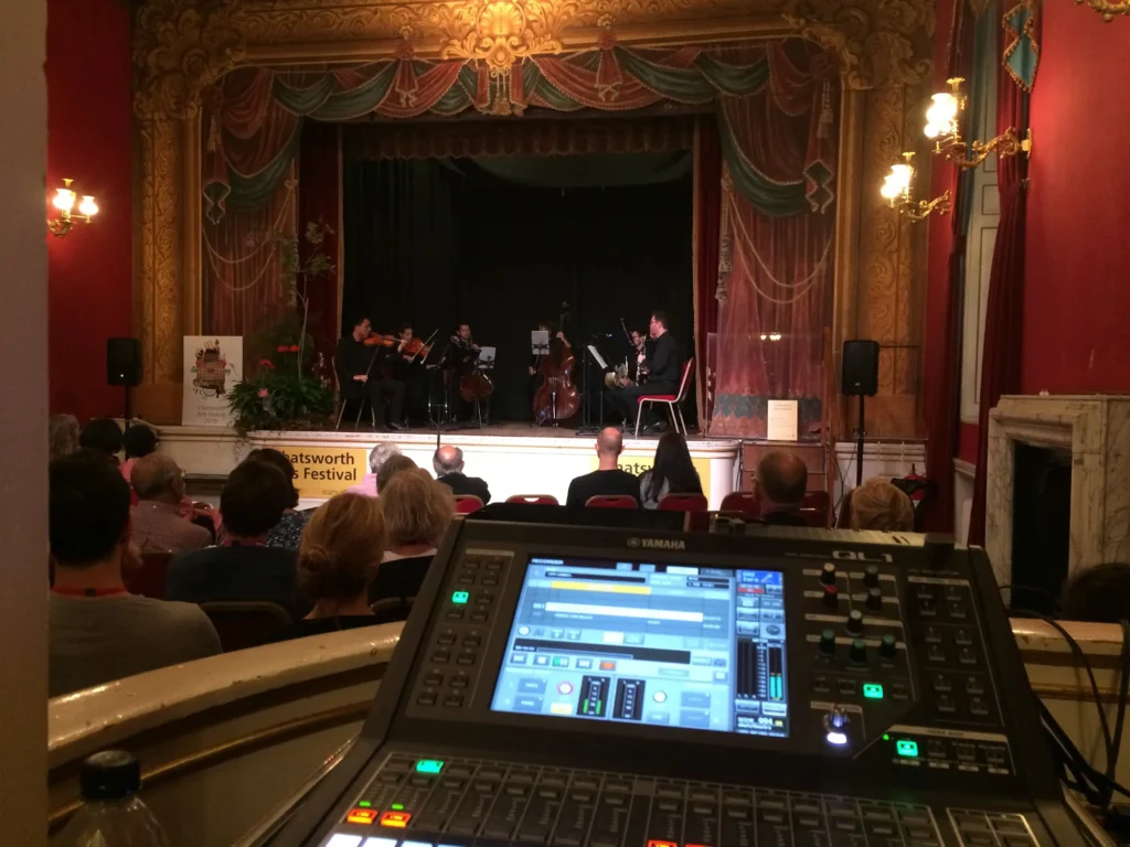 Chineke Orchestra performing on stage at Chatsworth Arts Festival. View from behind a Yamaha QL1 digital mixing console operated by sound engineer Jamie Rhodes-Simpson.