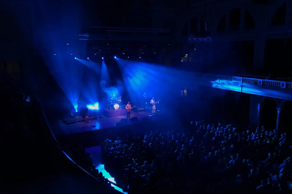 New Purple Celebration - the music of Prince perform at Hull City Hall. The view is from high up in the balcony. Blue moving lights look spectacular and can be seen streaming across the stage and over the very full audience.